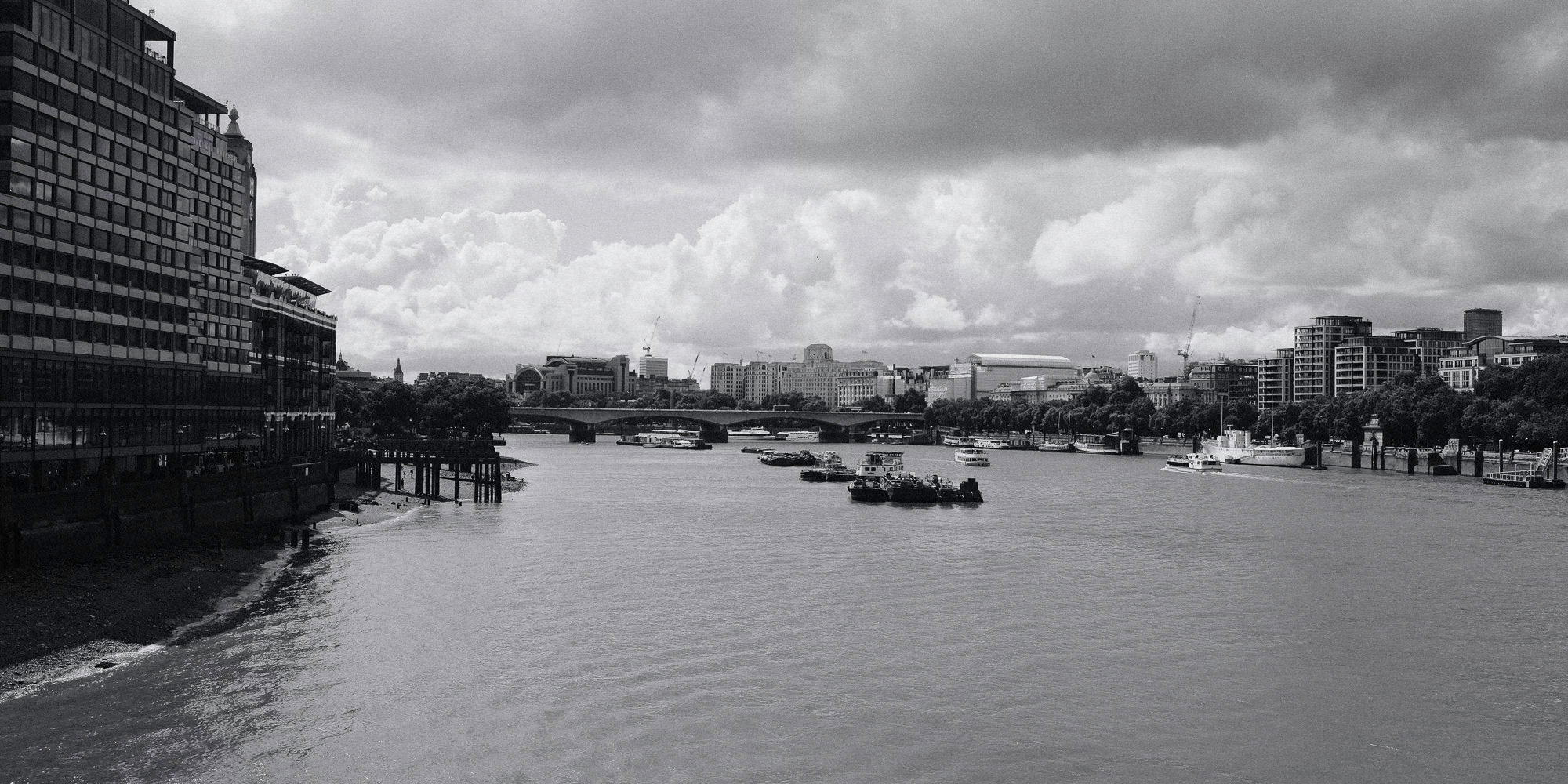 the river thames from the perspective of Blackfriars Bridge with some boats in the middle and looking onto another bridge in the background